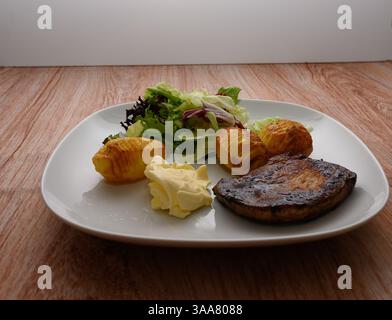 Un pasto ben organizzato presenta un pezzo di carne alla griglia accanto a patate arrosto dorate condite con spezie Foto Stock
