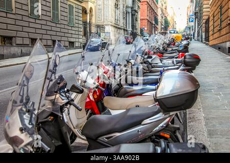 Gli scooter si allineavano lungo una strada a destra a Genova, Italia. Le case e la strada sono visibili. Foto Stock
