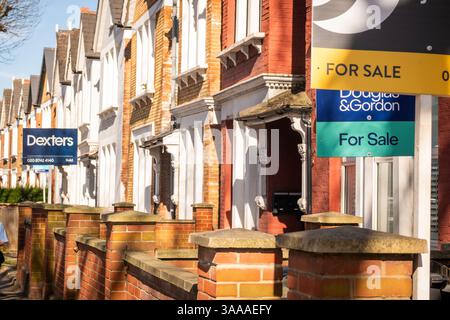 LONDRA - 31 MARZO 2025: L'agente immobiliare firma case pubblicitarie in vendita su file di case terrazzate in mattoni rossi nella zona di Clapham Balham nel sud-ovest di Londra Foto Stock