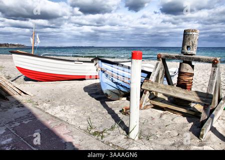 Una barca rossa e bianca è parcheggiata sulla spiaggia sabbiosa accanto a una barca blu del Mar Baltico in Germania. La barca rossa è posizionata sul lato sinistro della b blu Foto Stock