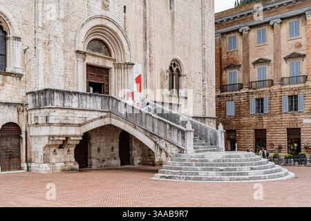 Un edificio in pietra con una bandiera rossa e bianca sul fronte a Gubbio, Umbria. L'edificio ha una scala in pietra che conduce al fronte Foto Stock