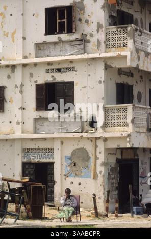 1 agosto 1992; Mogadiscio, SOMALIA; Un uomo somalo siede fuori da un ristorante in un edificio che mostra segni di colpi di mortaio e fori di proiettile nella terra di nessuno tra le due fazioni in guerra nel centro di Mogadiscio. Credito obbligatorio: Foto di Cheryl Hatch/ZUMA Press. (©) Copyright 1992 di Cheryl Hatch Foto Stock