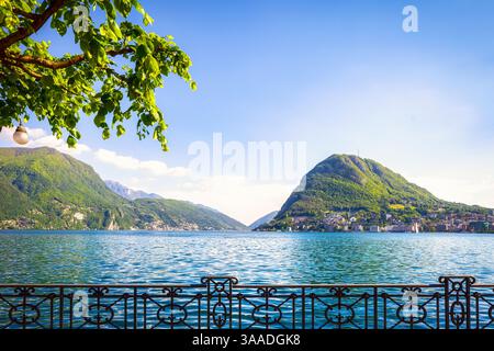 Terrazza e albero sul lago di Lugano con montagne sullo sfondo. Lugano, Cantone del Ticino, Svizzera o Confederazione Svizzera, Europa Foto Stock