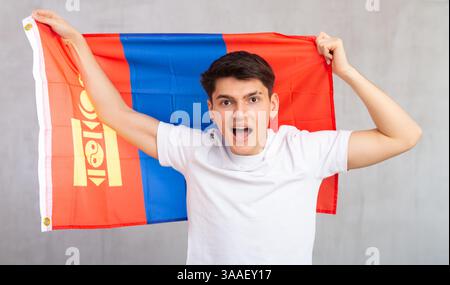 Eccitato, attivo spettatore maschile tiene bandiera nazionale della Mongolia in mani e canti slogan Foto Stock