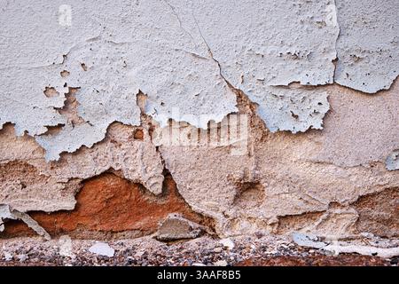 Pareti intemprate con vernice spaccata e staccata che deteriorano l'intonaco, esponendo vecchi mattoni, simboleggiando il decadimento e l'invecchiamento. Copia spazio Foto Stock