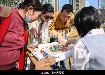 (250401) -- WUHAN, 1 aprile 2025 (Xinhua) -- le persone vedono un ricamo di Ren Wei in un parco vicino allo studio di Ren Wei a Wuhan, nella provincia di Hubei, nella Cina centrale, 19 marzo 2025. Il ricamo Han, un ricamo tradizionale con una storia di oltre 2.000 anni, è stato elencato come uno dei patrimoni culturali immateriali nazionali nel 2008. Famoso per le sue cuciture ruvide, i colori ricchi e i motivi audaci, spesso delinea i motivi del ricamo con linee oro o argento, offrendo un magnifico impatto visivo. Ren Wei, nato in una famiglia di ricami Han, è un erede rappresentativo dell'arte. Da quando lei W Foto Stock
