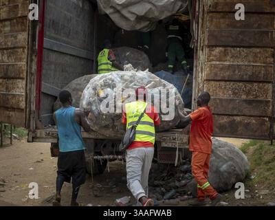 Il bordo di un letto di fiume a Douala. Rifiuti, inclusi bottiglie di plastica, sacchetti e detriti. I lavoratori e i collettori sono impegnati nel riciclo dei rifiuti di plastica in f Foto Stock