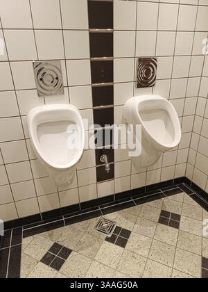 Bagno pubblico con piastrelle bianche e nere e due orinatoi sul muro Foto Stock