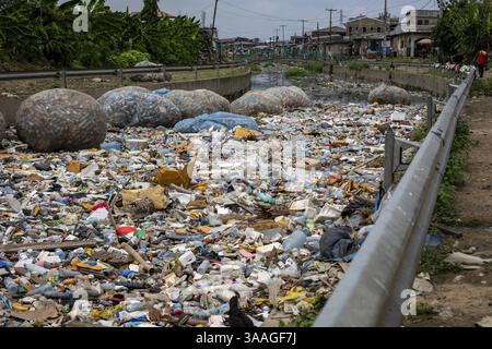 Fiume a Douala con varie forme di rifiuti, tra cui bottiglie di plastica, sacchetti e macerie. Inquinamento ambientale, rifiuti di plastica. Zona residenziale, urb Foto Stock