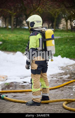 Un vigile del fuoco che indossa indumenti protettivi completi, tra cui un casco, una tuta ignifuga, guanti e un autorespiratore (SCBA), si distingue per Foto Stock