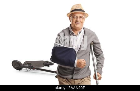 Uomo anziano con un braccio rotto e una stampelle che si sta riprendendo dopo un incidente con uno scooter elettrico isolato su sfondo bianco Foto Stock