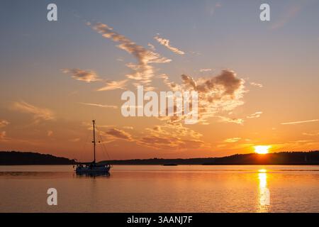 Barca a vela all'ancora nelle acque di bodden tra il porto di Barhöft e l'isola di Bock al tramonto nel Parco nazionale dell'area della laguna della Pomerania occidentale, Vorpommern-Rügen Foto Stock