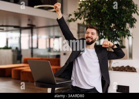 Eccitato gridare giovane uomo guardando lo schermo del suo computer e trionfare con le mani sollevate Foto Stock