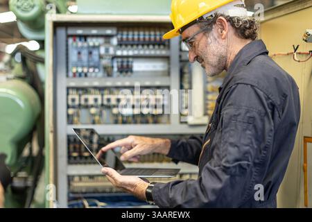Senior Professional Electrician ingegnere supervisore servizio controllo manutenzione macchina industria pesante cavo elettrico con computer portatile. Foto Stock