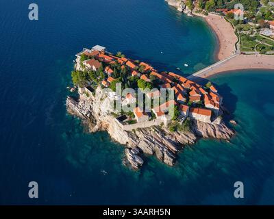 VISTA AEREA. Hotel a cinque stelle costruito su un'isola legata, raggiungibile da un tombolo sabbioso. Sveti Stefan, Montenegro. Foto Stock