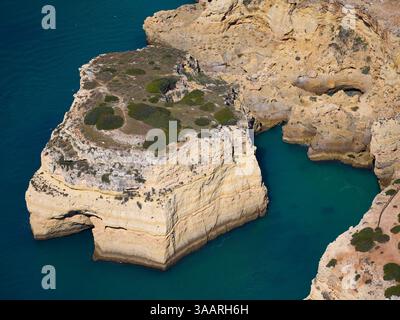 VISTA AEREA. Costa rocciosa frastagliata vicino a Farol de Alfanzina. Carvoeiro, Algarve, Portogallo. Foto Stock