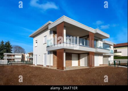 Nuova casa moderna con giardino privato sotto il cielo blu, dotata di balcone con ringhiera in legno e vetro Foto Stock