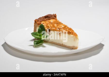Deliziosa fetta di Cheesecake fatta in casa guarnita con salsa al caramello e menta su piatto bianco. Foto Stock