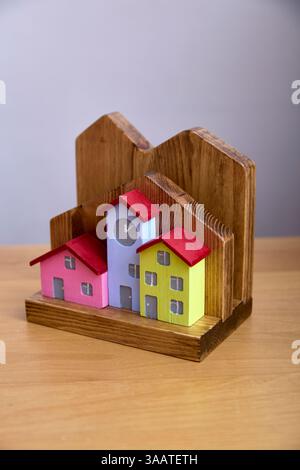 Colorato modello di casa in legno caratterizzato da una torre dell'orologio centrale. Questo oggetto decorativo aggiunge fascino ai tetti e alle finestre luminosi, ideali per la casa o per il tempo libero Foto Stock