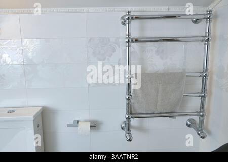 Bagno moderno con portasciugamani cromato e asciugamano sospeso. Piastrelle eleganti con motivi floreali. Spazio igienico e funzionale ideale per la casa Foto Stock