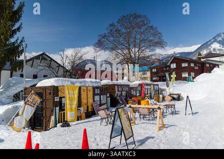Piccole cabine per cibo e bevande si siedono sulla neve in una giornata di sole alla stazione sciistica di Tsugaike, Nagano, Giappone Foto Stock