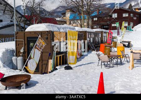 Piccole cabine per cibo e bevande si siedono sulla neve in una giornata di sole alla stazione sciistica di Tsugaike, Nagano, Giappone Foto Stock
