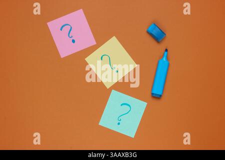 Appunti di carta con punti interrogativi disegnati, pennarello su sfondo marrone. Vista dall'alto Foto Stock