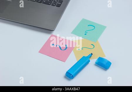 Laptop, fogli di carta con punti interrogativi disegnati e pennarello su sfondo bianco. Vista dall'alto Foto Stock