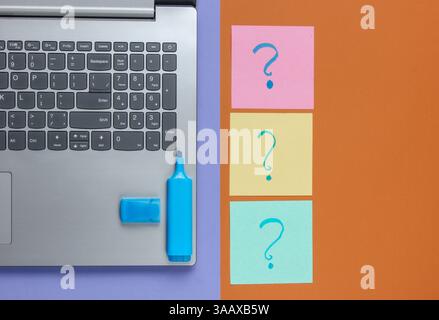 Laptop, fogli di carta con punti interrogativi disegnati e pennarello su sfondo marrone viola. Vista dall'alto Foto Stock