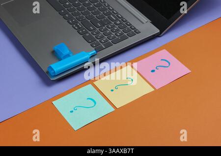 Laptop, fogli di carta con punti interrogativi disegnati e pennarello su sfondo marrone viola. Vista dall'alto Foto Stock