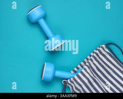 Borsa sportiva a righe con manubri su sfondo blu. Sport natura morta. Vista dall'alto. Foto Stock