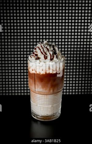 Caffè freddo con panna montata e cioccolato in un bicchiere su sfondo nero Foto Stock