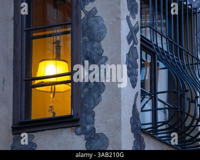 Una finestra illuminata con una lampada incandescente all'interno di una vecchia casa medievale a Innsbruck, circondata da pareti decorative e barre metalliche sulla finestra adiacente Foto Stock