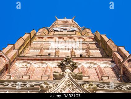 Una vista dall'angolo basso di un alto campanile in mattoni della basilica di San Martino a Landshut contro un cielo azzurro. Foto Stock