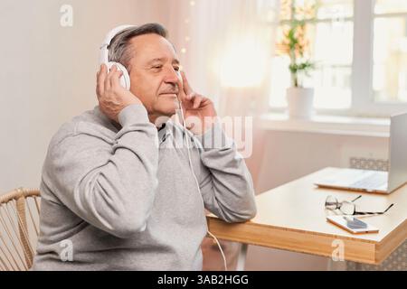 Uomo anziano che si rilassa a casa con le cuffie, ascolta un audiobook o un podcast. Relax, tempo libero e temi audio Foto Stock