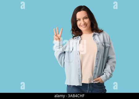 Bella donna matura felice che mostra tre dita su sfondo blu Foto Stock
