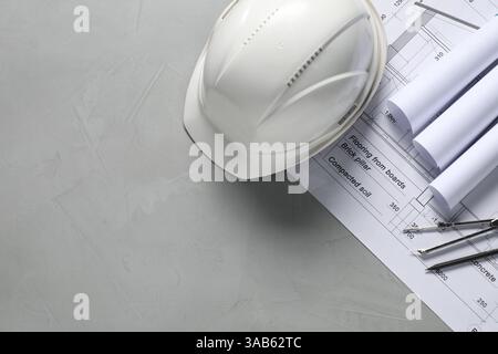 Diversi disegni architettonici, elmetto, matita e divisore su tavolo grigio, piatto. Spazio per il testo Foto Stock
