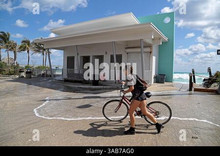 6 marzo 2018 - Dania Beach, Florida, Stati Uniti - Un ciclista cammina accanto a un bagno pubblico a Dania Beach dove onde e sabbia fluiscono nel parcheggio martedì 6 marzo 2018 a Dania Beach, Flag. Le ondate dell'oceano continuano a spingersi sulla costa della Florida meridionale facendo sì che la città chiuda il parcheggio di Dania Beach da Dania Beach Blvd. Al molo. (Immagine di credito: © Susan Stocker/TNS via ZUMA Wire) Foto Stock
