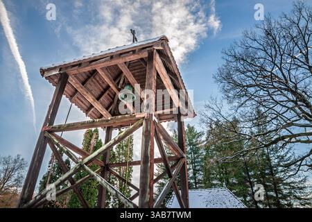 Una campana serba ortodossa all'interno di un tradizionale campanile in legno, adagiata su un cielo sereno e un paesaggio innevato nella campagna serba. Foto Stock