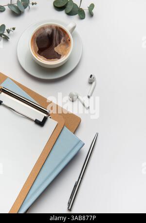 Scrivania da ufficio con caffè, eucalipto, appunti, notebook, penna, e cuffie wireless per una giornata produttiva Foto Stock