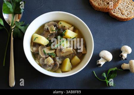 Gustosa zuppa con funghi champignon, patate ed erbe aromatiche in una ciotola bianca. Cibo sano e vegetariano. Direttamente sopra. Foto Stock