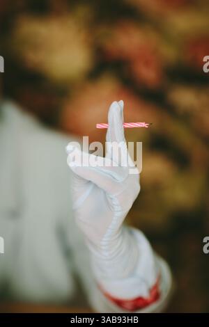 Un'immagine ravvicinata cattura una mano con i guanti che regge delicatamente una piccola candela di compleanno illuminata. L'ambientazione suggerisce un ambiente da studio con un'atmosfera calda e soffice Foto Stock