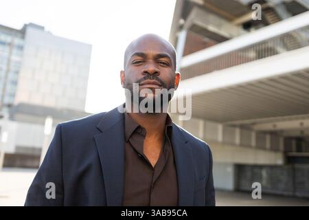 Un cubano con un abito scuro si trova all'aperto in un ambiente urbano. L'immagine cattura determinazione e professionalità, con un dorso architettonico moderno Foto Stock