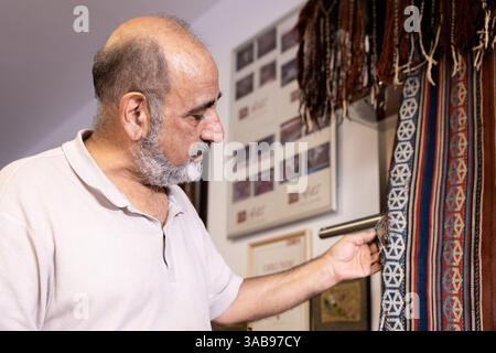 Un maestro iraniano esamina e ripristina tappeti rari nel suo laboratorio ben attrezzato situato a Salisburgo, Austria, circondato da strumenti e tradizionali Foto Stock