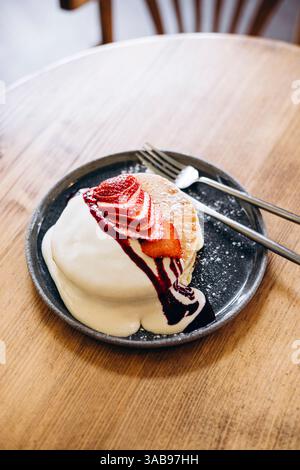 Soffici pancake giapponesi ricoperti di fragole a fette, salsa cremosa e sciroppo su un piatto rotondo. Il delizioso dessert è presentato elegantemente, impostato Foto Stock
