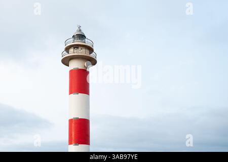 A Fuerteventura, nelle Isole Canarie, si erge un impressionante faro rosso e bianco che si erge su un cielo soffice e nuvoloso, catturando la serena bellezza della lan estiva Foto Stock