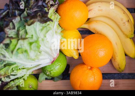 Una vivace esposizione di frutta e verdura, tra cui lattuga, arance, banane, limes, e limoni, disposti su un tavolo di legno. Perfetto per una sana ea Foto Stock