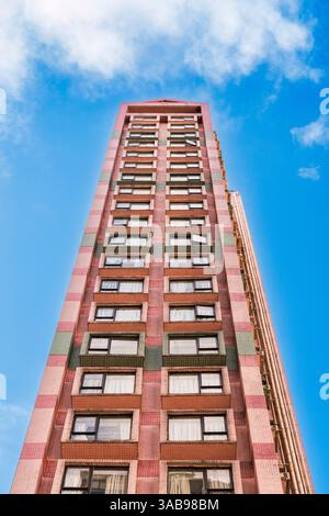 Da sotto un alto edificio residenziale a Hong Kong, evidenziato da un cielo azzurro. L'edificio presenta un mix di facciate di piastrelle rosa e verdi, con Foto Stock