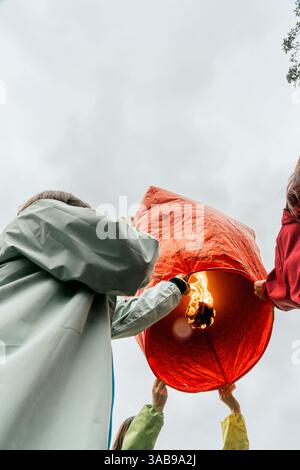 Dal basso persone irriconoscibili a Taiwan che sollevano una lanterna cinese rossa brillante pronta per il volo. Partecipanti, rivestiti di impermeabili, preparate questo lante Foto Stock