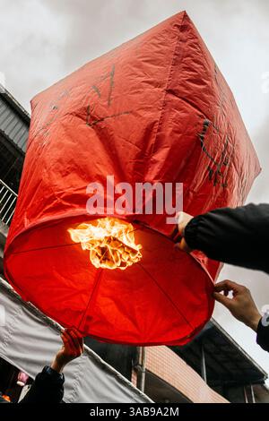 Vista a basso angolo di una persona irriconoscibile che rilascia una grande lanterna cinese rossa a Taiwan, piena di benedizioni scritte e desideri di salute, happi Foto Stock